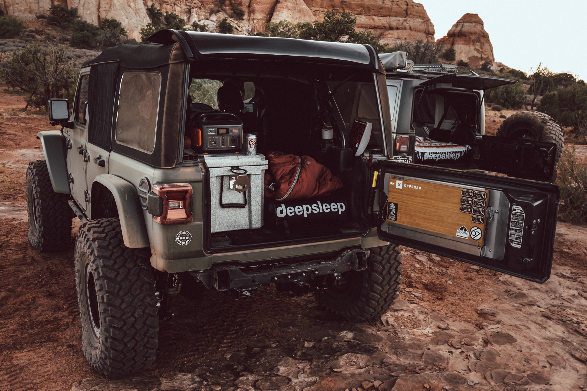 Deepsleep car camping mattress with overland camping gear in the back of a 4-door Jeep in the desert surrounded by rugged mountains.