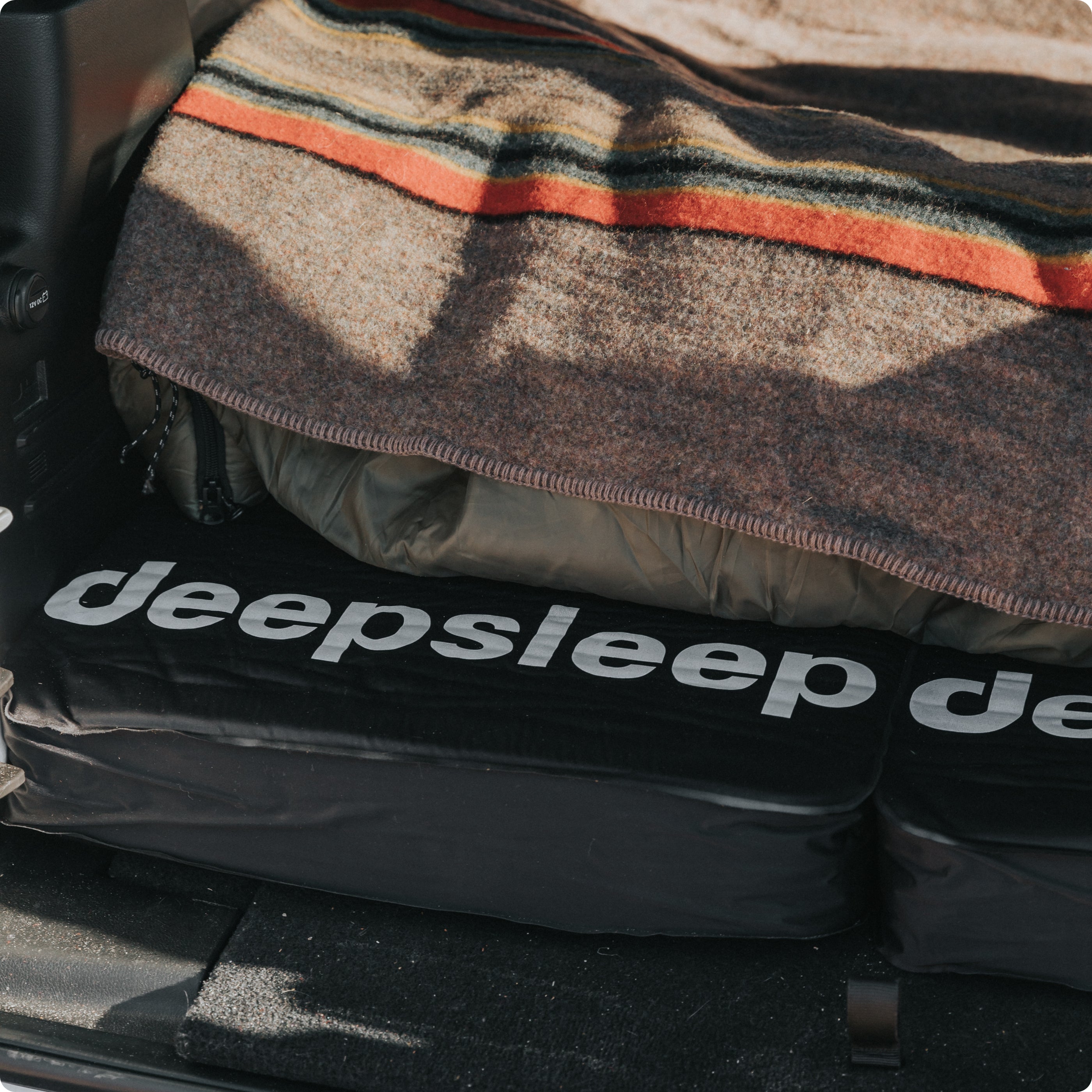 Closeup of Deepsleep logo on two solo foam mattresses with cozy bedding nestled in back of overland vehicle.